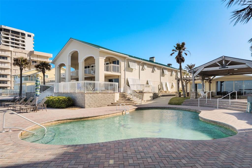 A swimming pool sits in front of a multi-story building with a covered patio area — 3837-3839 S ATLANTIC AVENUE, DAYTONA BEACH, FL
