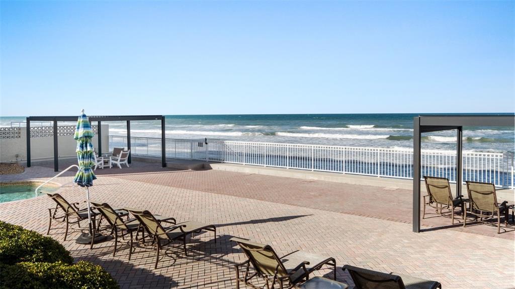 A paved pool deck features lounge chairs and a pergola overlooking the ocean — 3837-3839 S ATLANTIC AVENUE, DAYTONA BEACH, FL