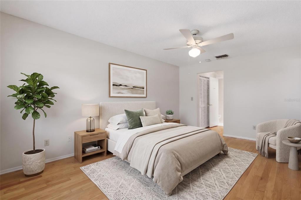 A bedroom features a bed with neutral bedding, a potted plant, and a corner chair — 2211 LARK CIRCLE W UNIT D, PALM HARBOR, FL