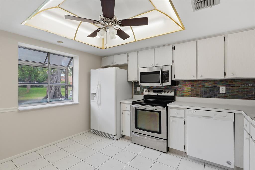 A kitchen features white cabinets, stainless steel appliances, a colorful tiled backsplash, and a ceiling fan — 2211 LARK CIRCLE W UNIT D, PALM HARBOR, FL