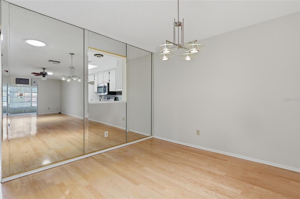 A dining area features light wood flooring, a modern chandelier, and a large mirrored wall — 2211 LARK CIRCLE W UNIT D, PALM HARBOR, FL