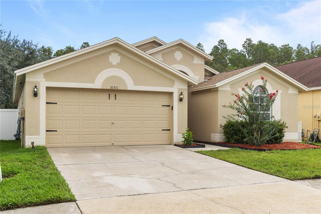 A single-story house with a beige stucco exterior, a two-car garage, and a front lawn — 31511 WRENCREST DRIVE, WESLEY CHAPEL, FL