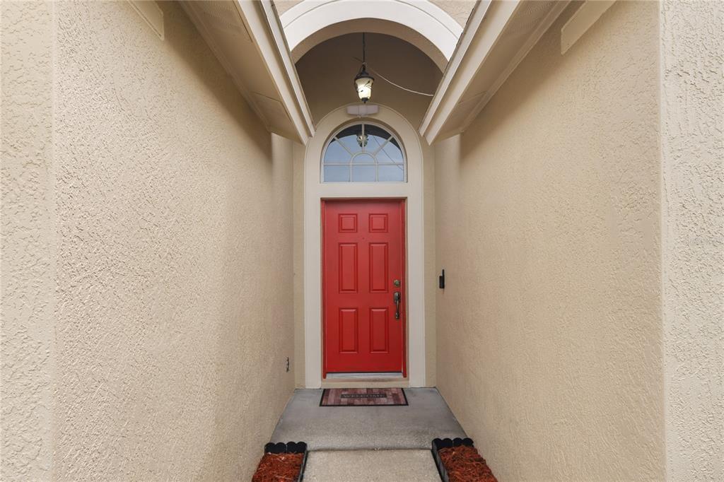 A bright red front door is framed by an arched entryway and beige stucco walls — 31511 WRENCREST DRIVE, WESLEY CHAPEL, FL