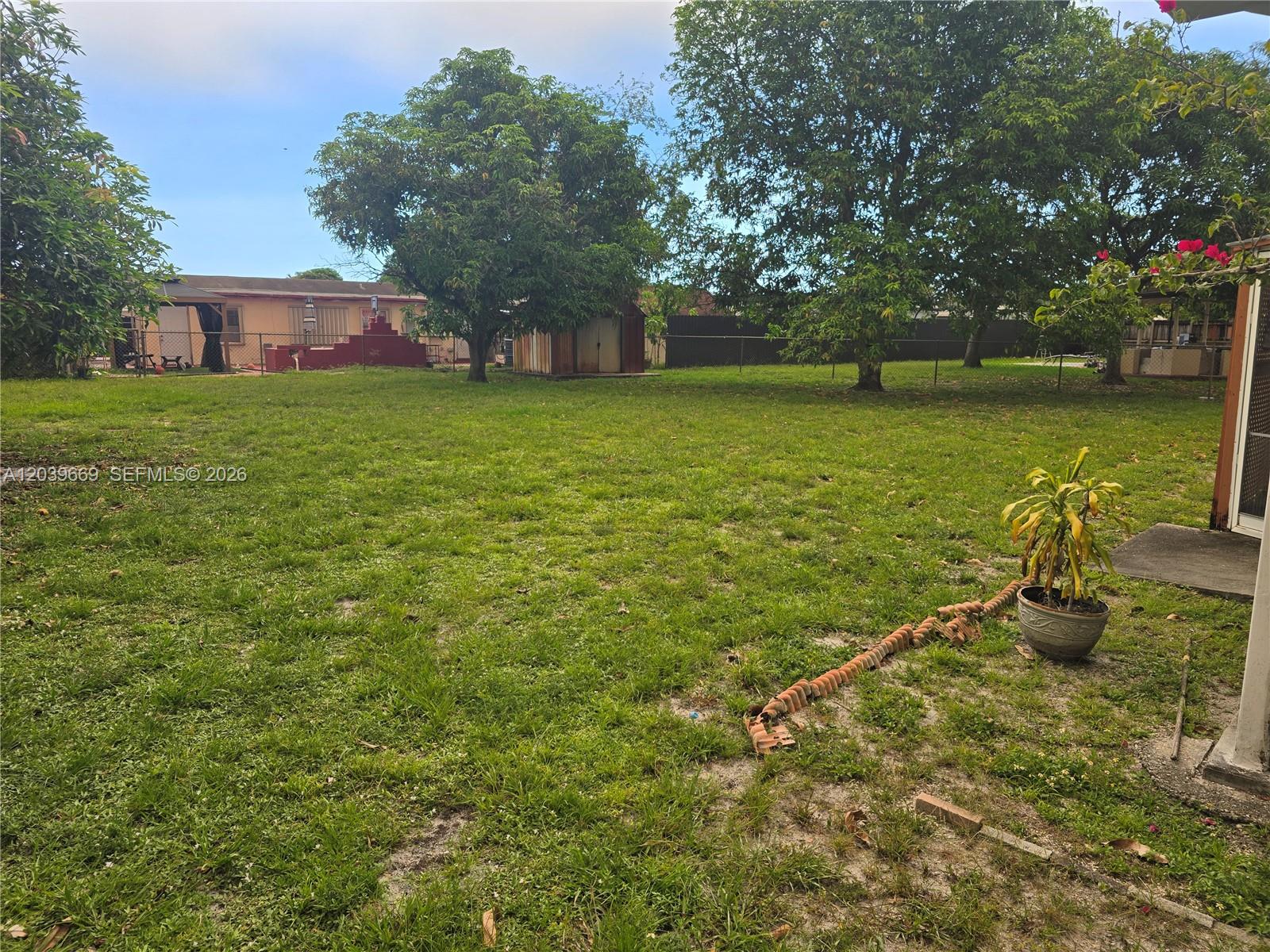 A large, grassy backyard features several mature trees, a small shed, and a fence — MIAMI GARDENS, FL