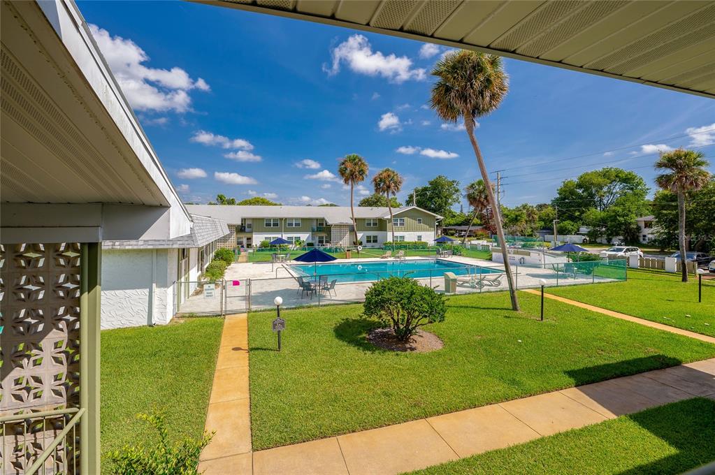 A view from a patio overlooking a swimming pool, green lawn, and apartment buildings — 840 CENTER AVENUE UNIT 100, HOLLY HILL, FL