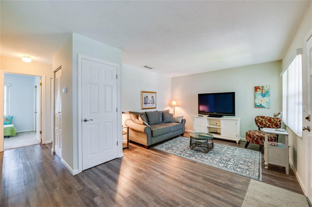 A living room features wood-look flooring, a gray sofa, a television, and a patterned armchair — 840 CENTER AVENUE UNIT 100, HOLLY HILL, FL