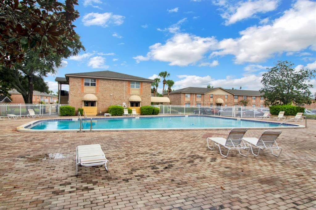 A brick apartment building overlooks a rectangular swimming pool with lounge chairs on a patio — 2422 BRANCH WAY UNIT 100, MAITLAND, FL