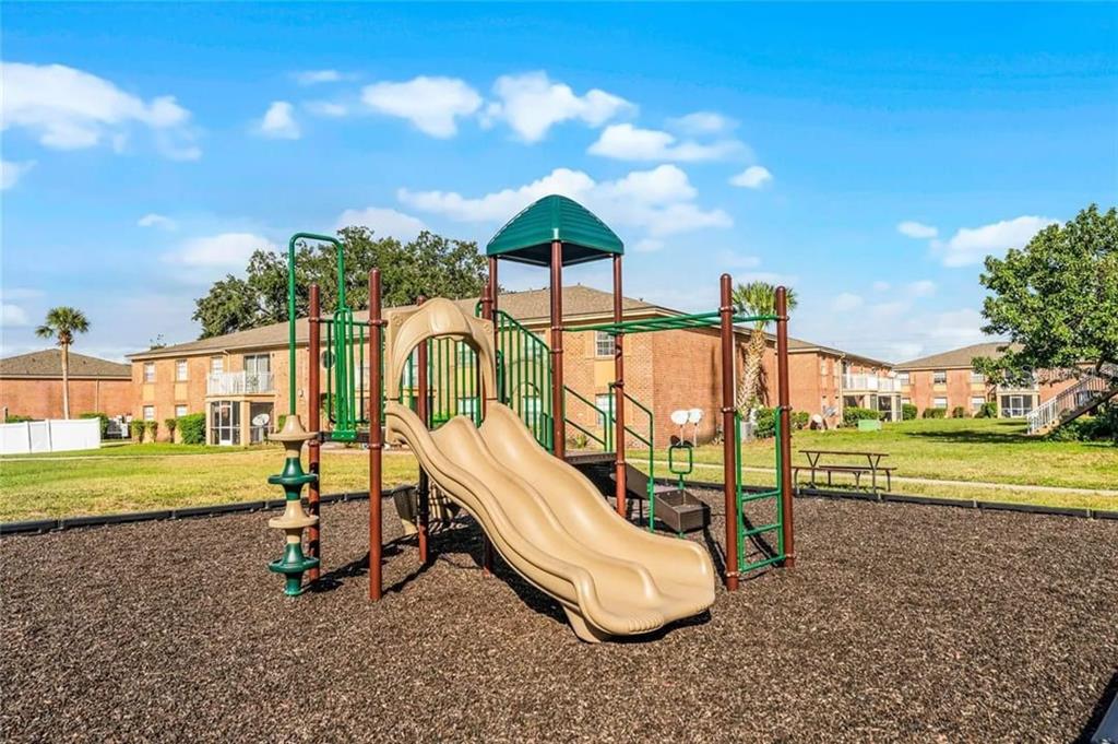 A playground with a tan slide and green climbing structure sits on a wood-mulched area — 2422 BRANCH WAY UNIT 100, MAITLAND, FL