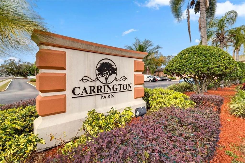 A beige monument sign with the text Carrington Park stands in a landscaped garden area — 2422 BRANCH WAY UNIT 100, MAITLAND, FL