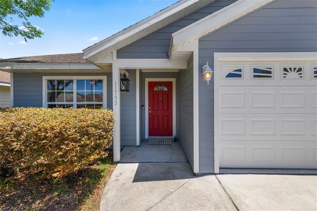 The exterior of a house features gray siding, a red front door, and a garage — 11753 NW 60TH TERRACE, ALACHUA, FL