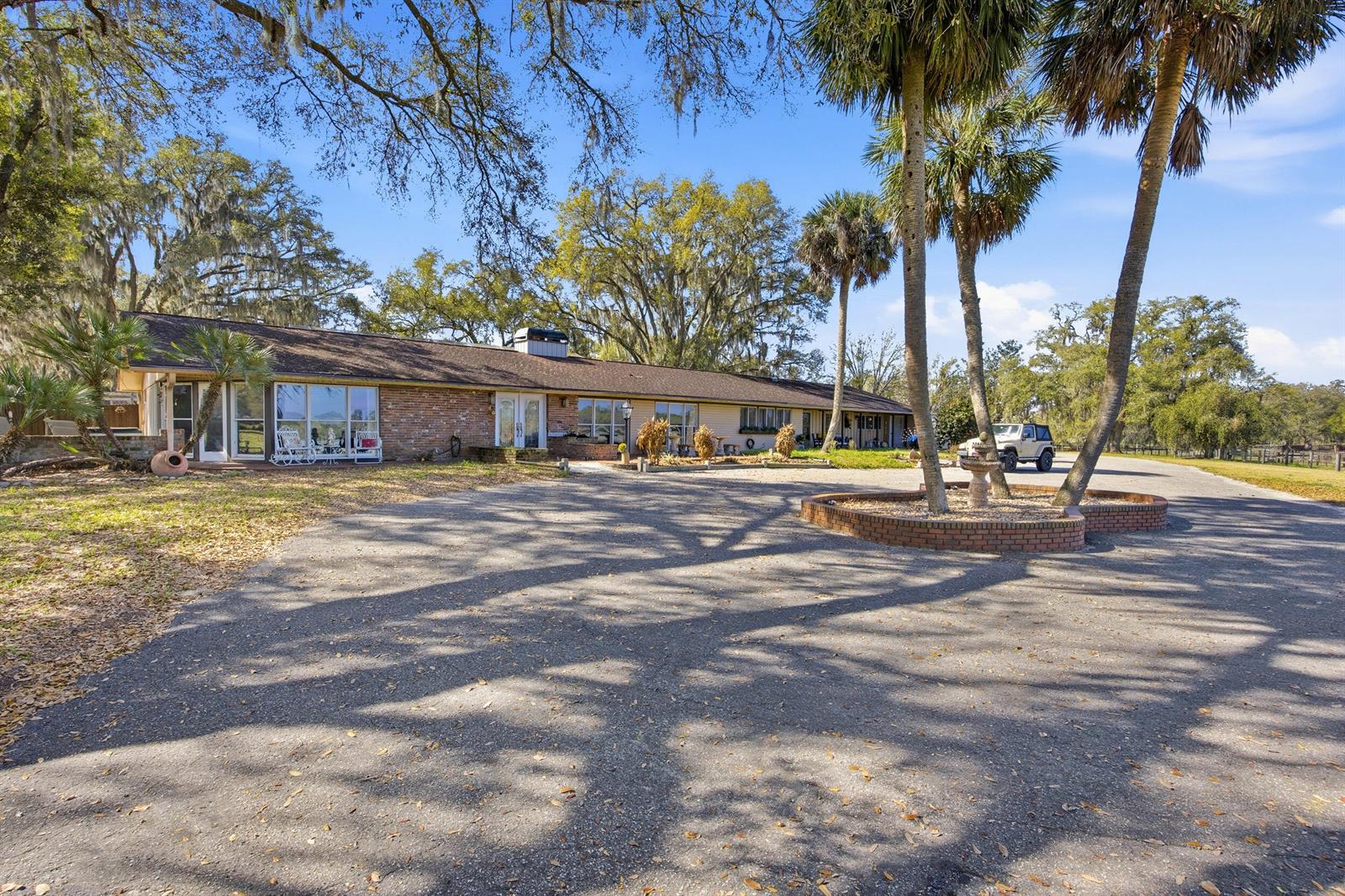 A long, single-story brick house sits behind a large paved driveway with palm trees — 6025 NW 115th Avenue, Ocala FL 34482, OCALA, FL