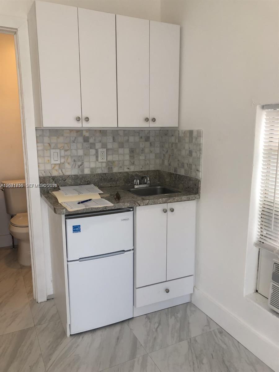 A small kitchenette features white cabinets, a granite countertop, a sink, and a mini-fridge — HOLLYWOOD, FL