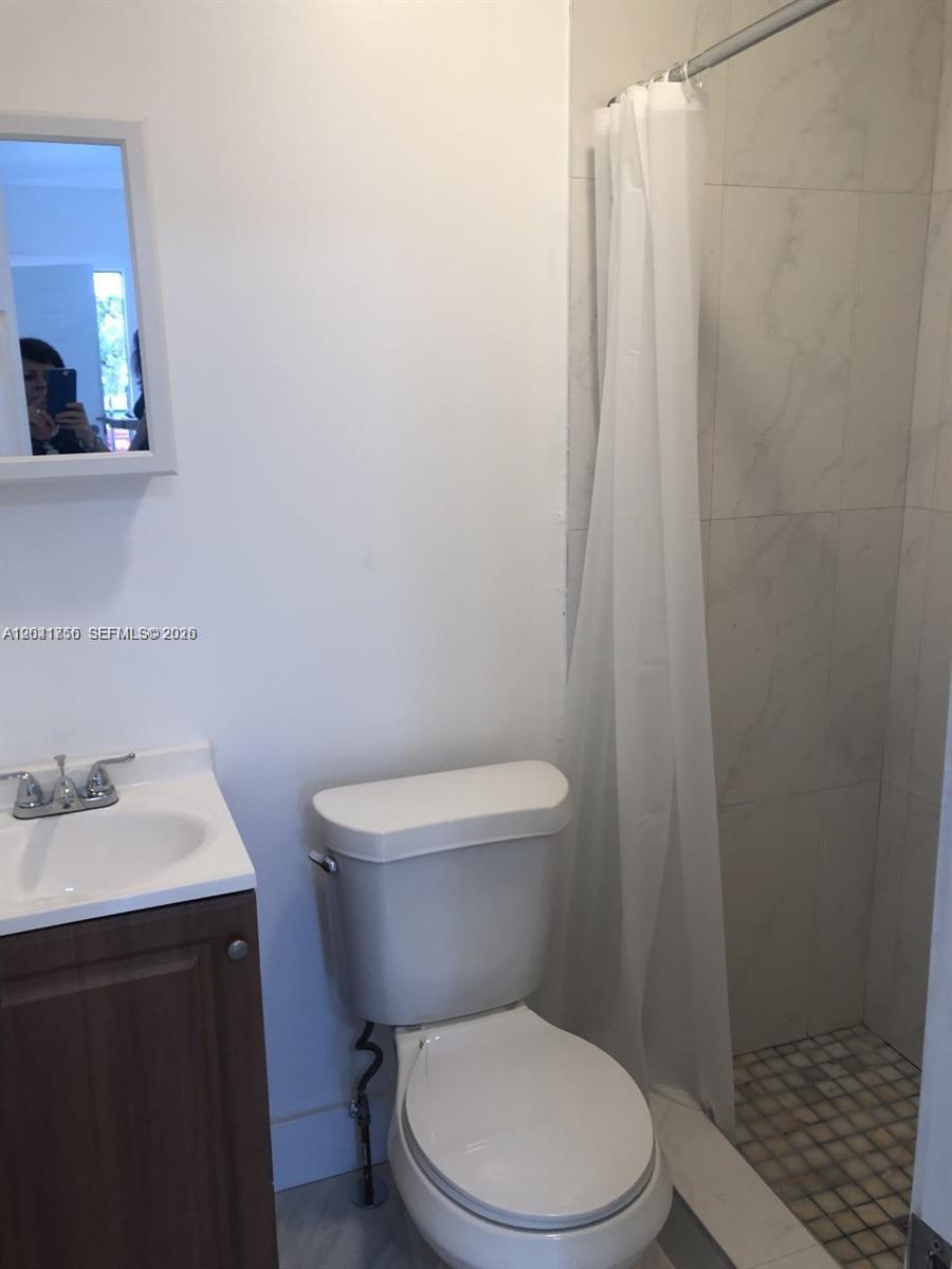 A bathroom features a vanity, a toilet, and a tiled shower stall with a curtain — HOLLYWOOD, FL