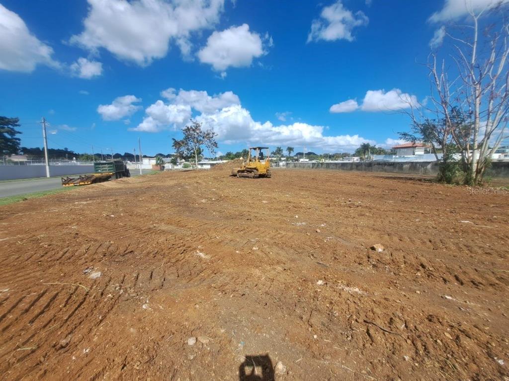 A bulldozer sits on a cleared, dirt-covered lot under a bright blue sky — CARRETERA #2 CANDELARIA WARD INTERIOR, TOA BAJA, PR