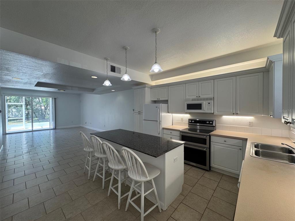 An open-concept living area with light-colored tile flooring leads into a white kitchen — 2053 GREEN OAK COURT, KISSIMMEE, FL
