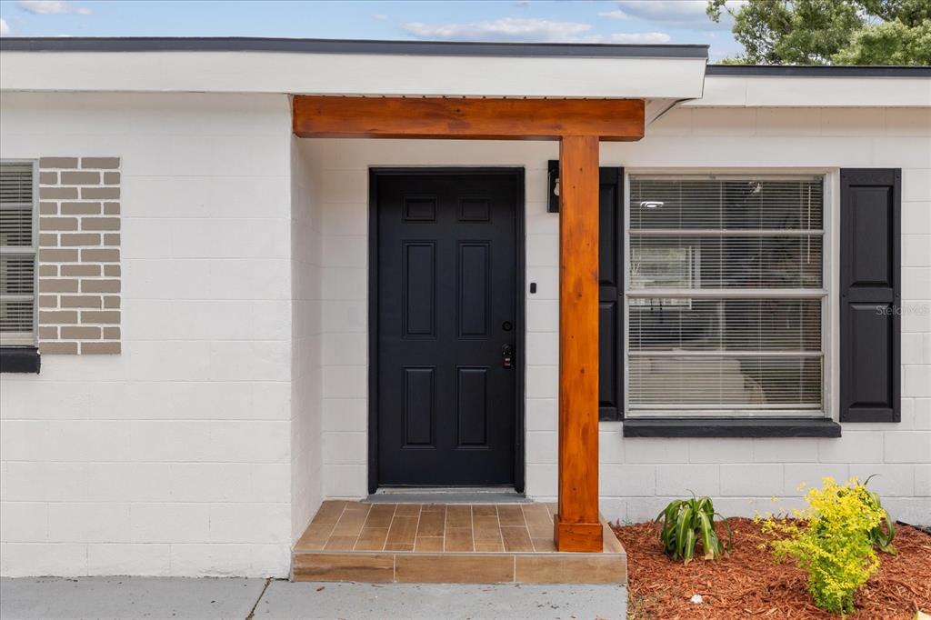 A white concrete block house exterior features a black front door and a wooden post — 4922 S 82ND STREET, TAMPA, FL