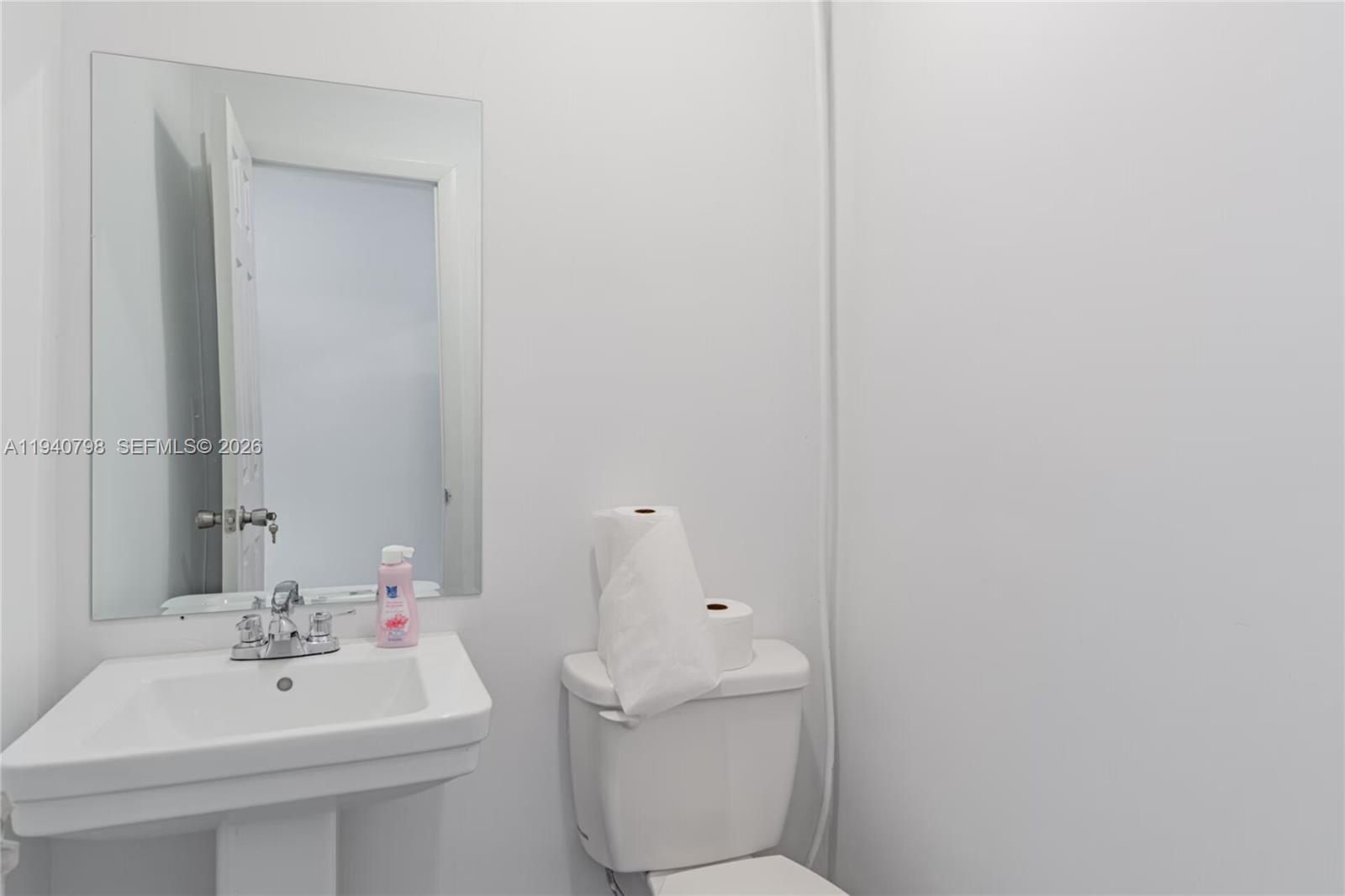 A small bathroom features a white pedestal sink, a toilet, and a wall-mounted mirror — 1670 W 31st Pl, Hialeah FL 33012, HIALEAH, FL