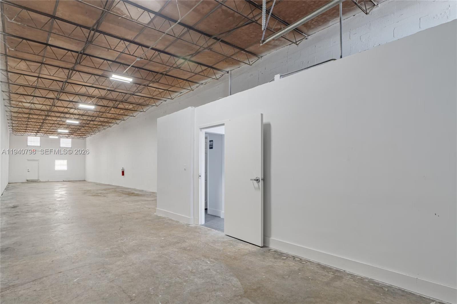 An open industrial warehouse space features a concrete floor, exposed ceiling trusses, and a restroom — 1670 W 31st Pl, Hialeah FL 33012, HIALEAH, FL