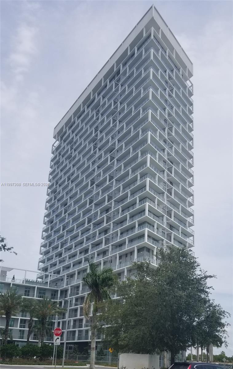 A tall, modern residential high-rise building features stacked balconies and a white exterior facade — 2000 Metropica Way # 505, Sunrise FL 33323, SUNRISE, FL