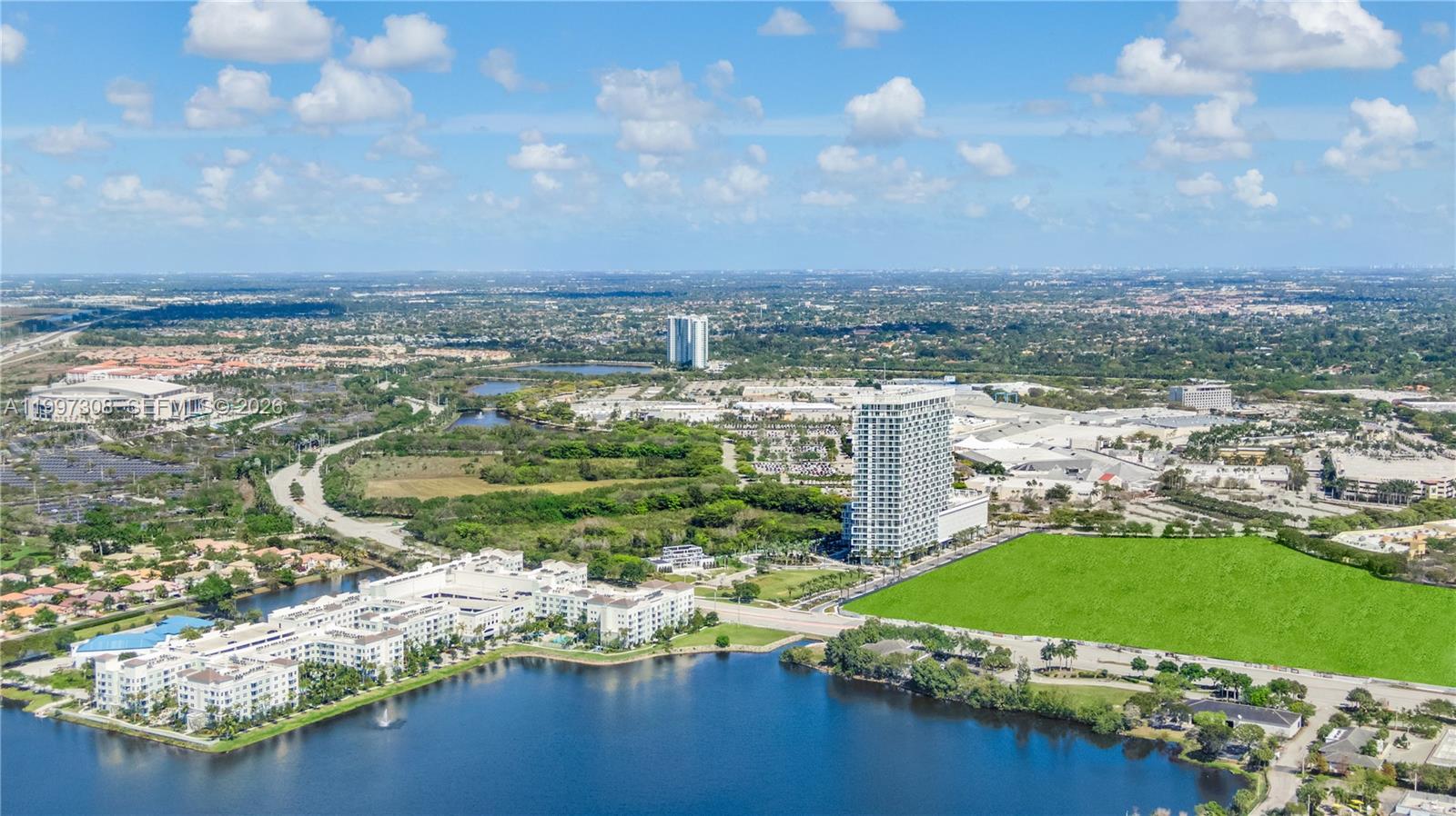 An aerial view shows a large apartment complex, a tall residential tower, and a lake — 2000 Metropica Way # 505, Sunrise FL 33323, SUNRISE, FL