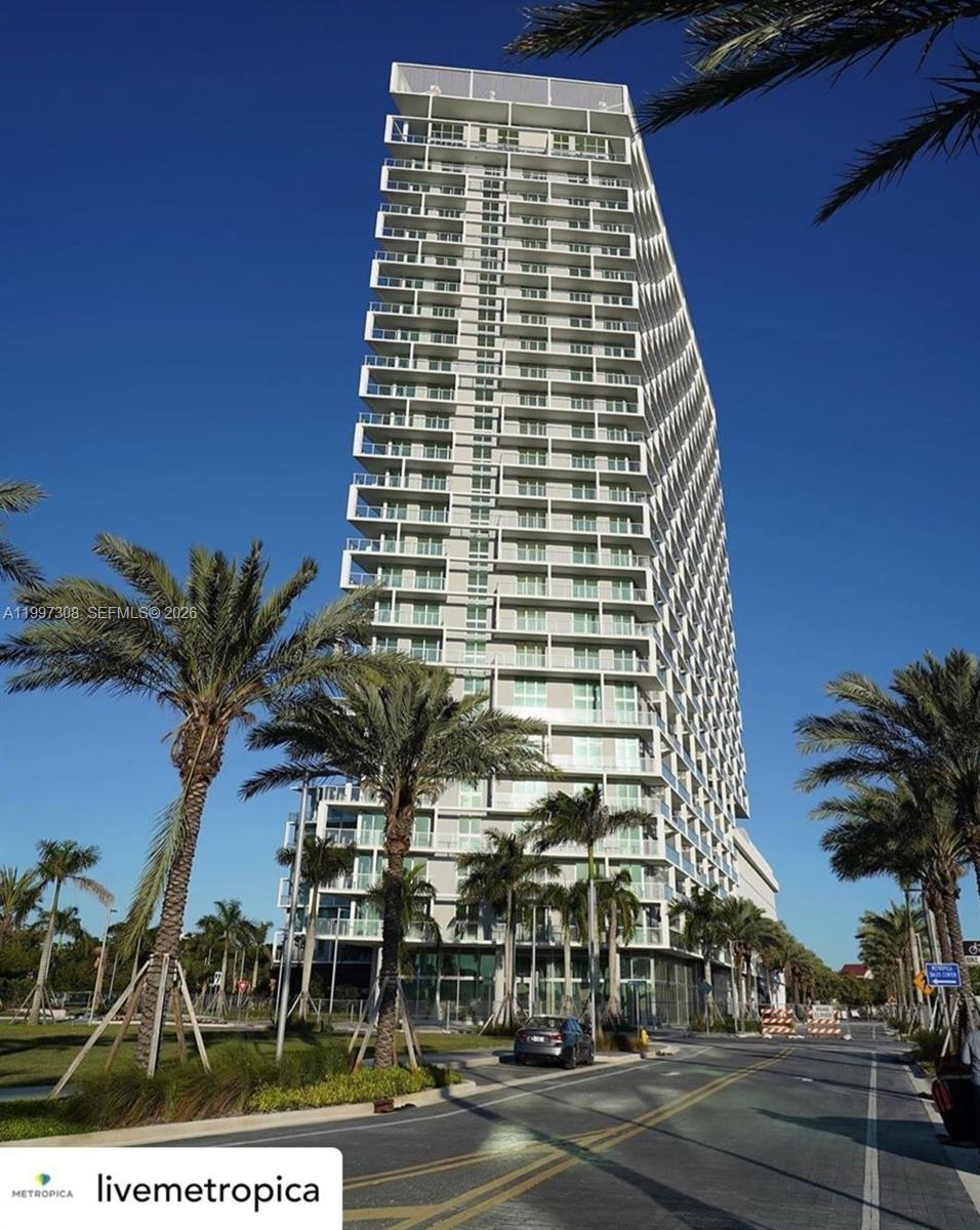 A tall, modern residential high-rise building stands under a clear blue sky — 2000 Metropica Way # 505, Sunrise FL 33323, SUNRISE, FL