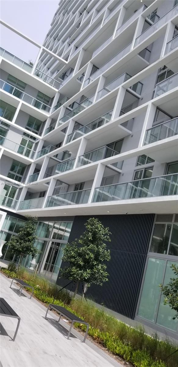 A low-angle view of a modern multi-story apartment building with glass balconies and landscaping — 2000 Metropica Way # 505, Sunrise FL 33323, SUNRISE, FL