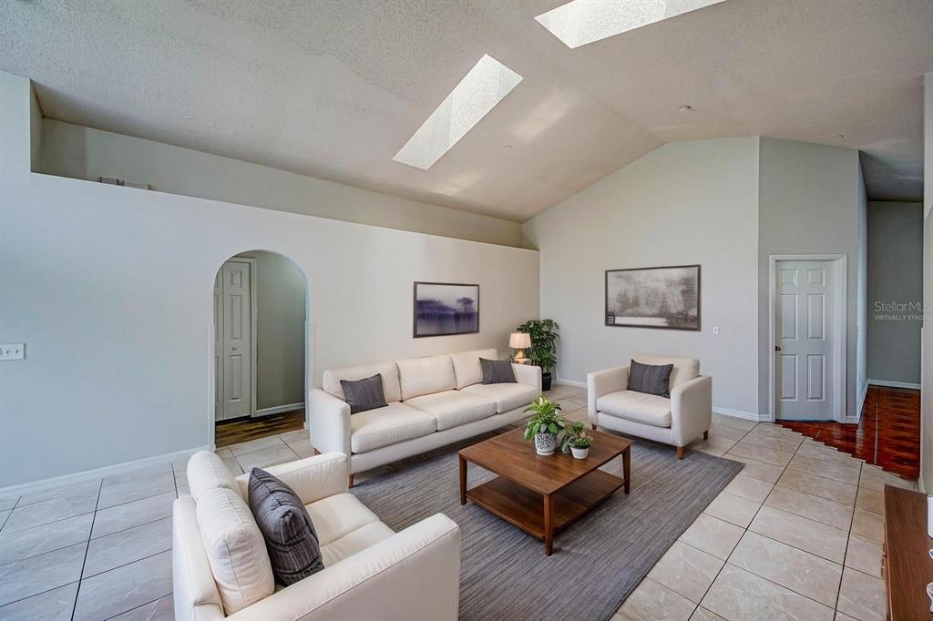 A living room features a vaulted ceiling with skylights, tile flooring, and neutral-colored furniture — 3 CECILIA WAY, KISSIMMEE, FL