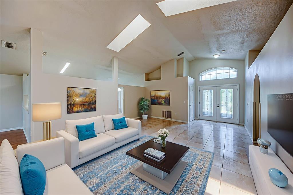 A living room features white sofas, a blue patterned rug, tile floors, and skylights — 3 CECILIA WAY, KISSIMMEE, FL