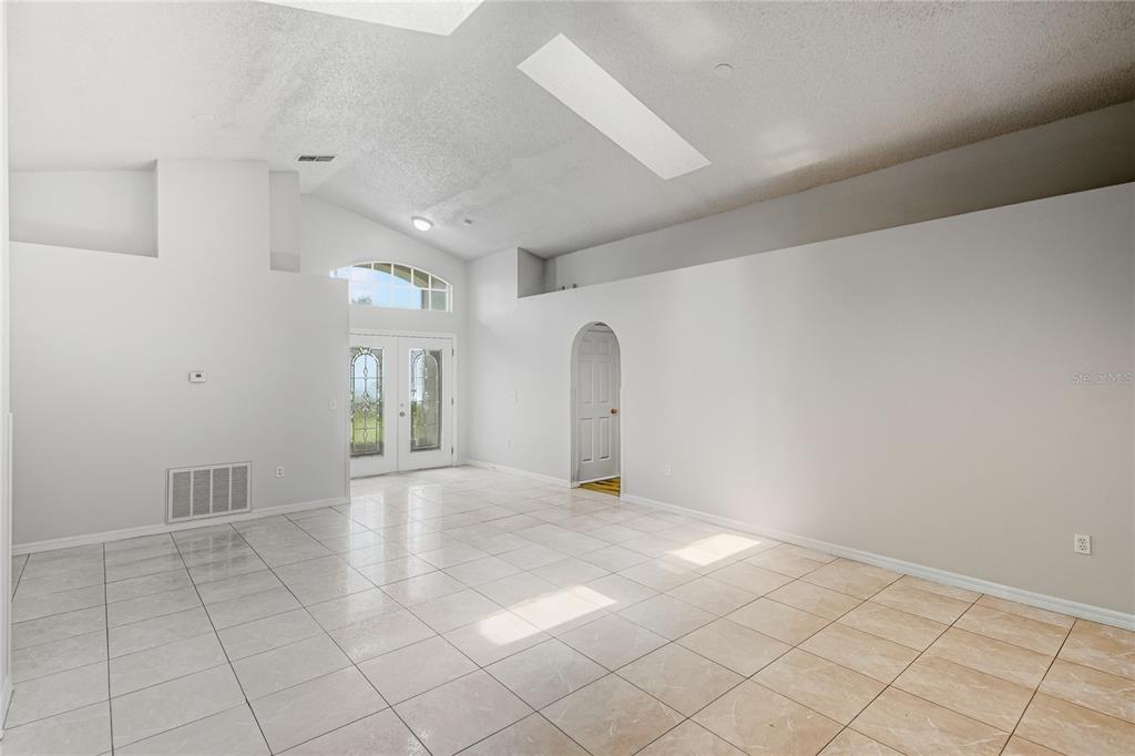 A bright, empty living room features vaulted ceilings, white walls, and light-colored tile flooring — 3 CECILIA WAY, KISSIMMEE, FL