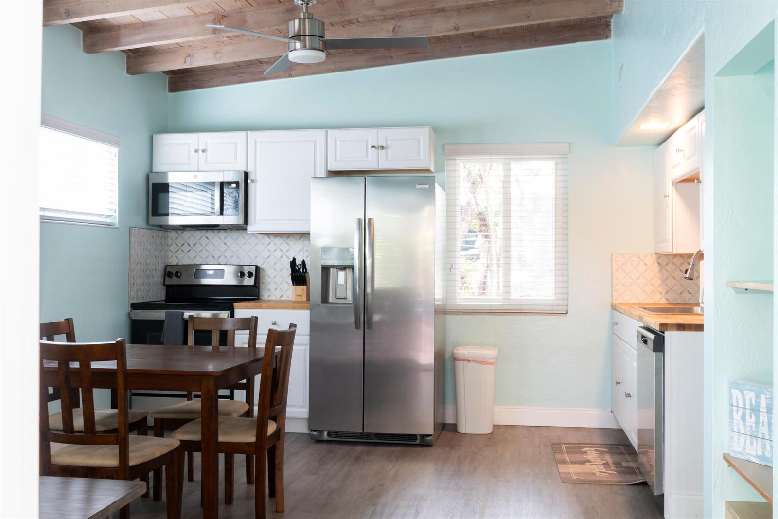 A kitchen features light blue walls, white cabinets, stainless steel appliances, and a wooden dining set — 204 Coral Road, Boynton Beach FL 33435, BOYNTON BEACH, FL