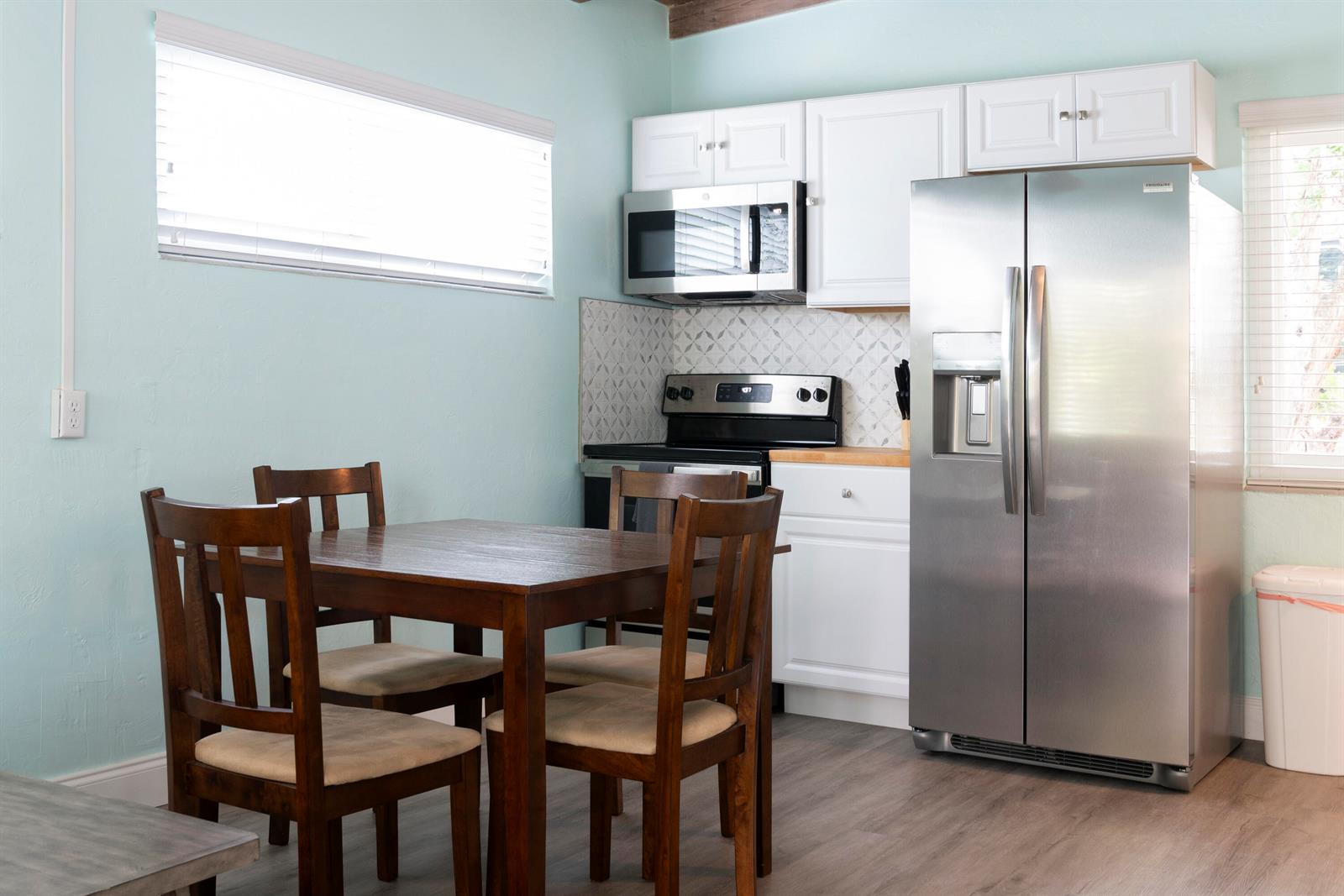 A kitchen with light blue walls, white cabinets, stainless steel appliances, and a wooden dining set — 204 Coral Road, Boynton Beach FL 33435, BOYNTON BEACH, FL