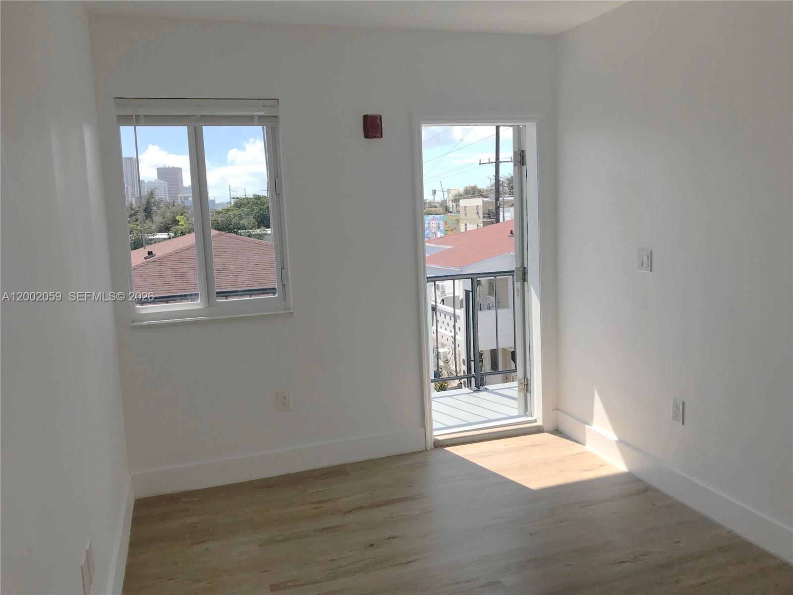 An empty room with white walls, light wood-look flooring, a window, and a balcony door — 1815 NW 1st CT # 8, Miami FL 33136, MIAMI, FL
