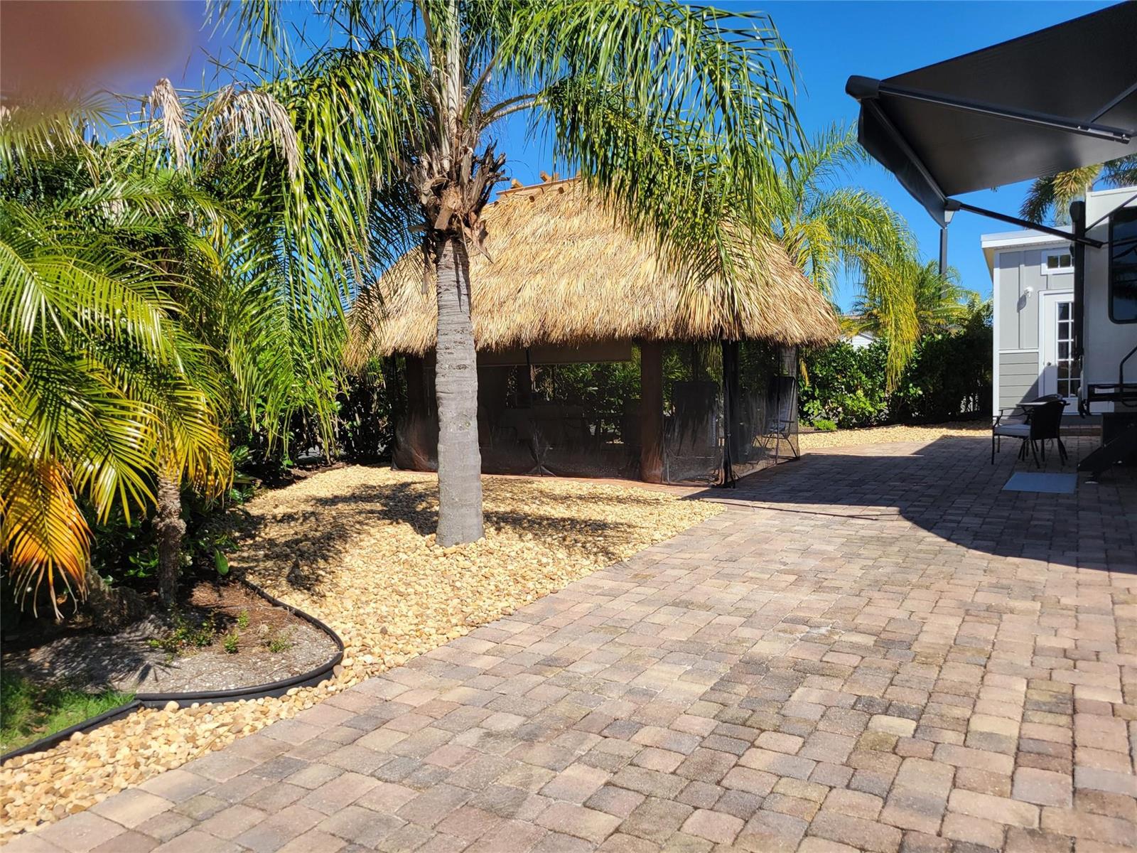 A thatched-roof tiki hut sits on a stone patio next to a palm tree — 545 SW 40th Cove, Okeechobee FL 34974, OKEECHOBEE, FL