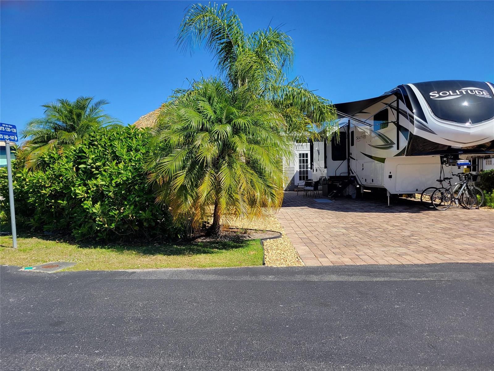 A large Solitude fifth-wheel RV is parked on a paved driveway next to palm trees — 545 SW 40th Cove, Okeechobee FL 34974, OKEECHOBEE, FL