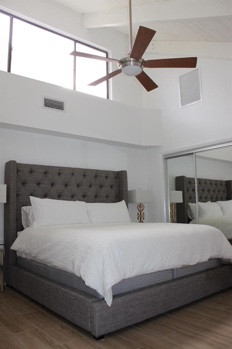A bedroom with a tufted gray headboard, white bedding, a ceiling fan, and mirrored closets — 1605 S Us Hwy One, Jupiter FL 33477, JUPITER, FL