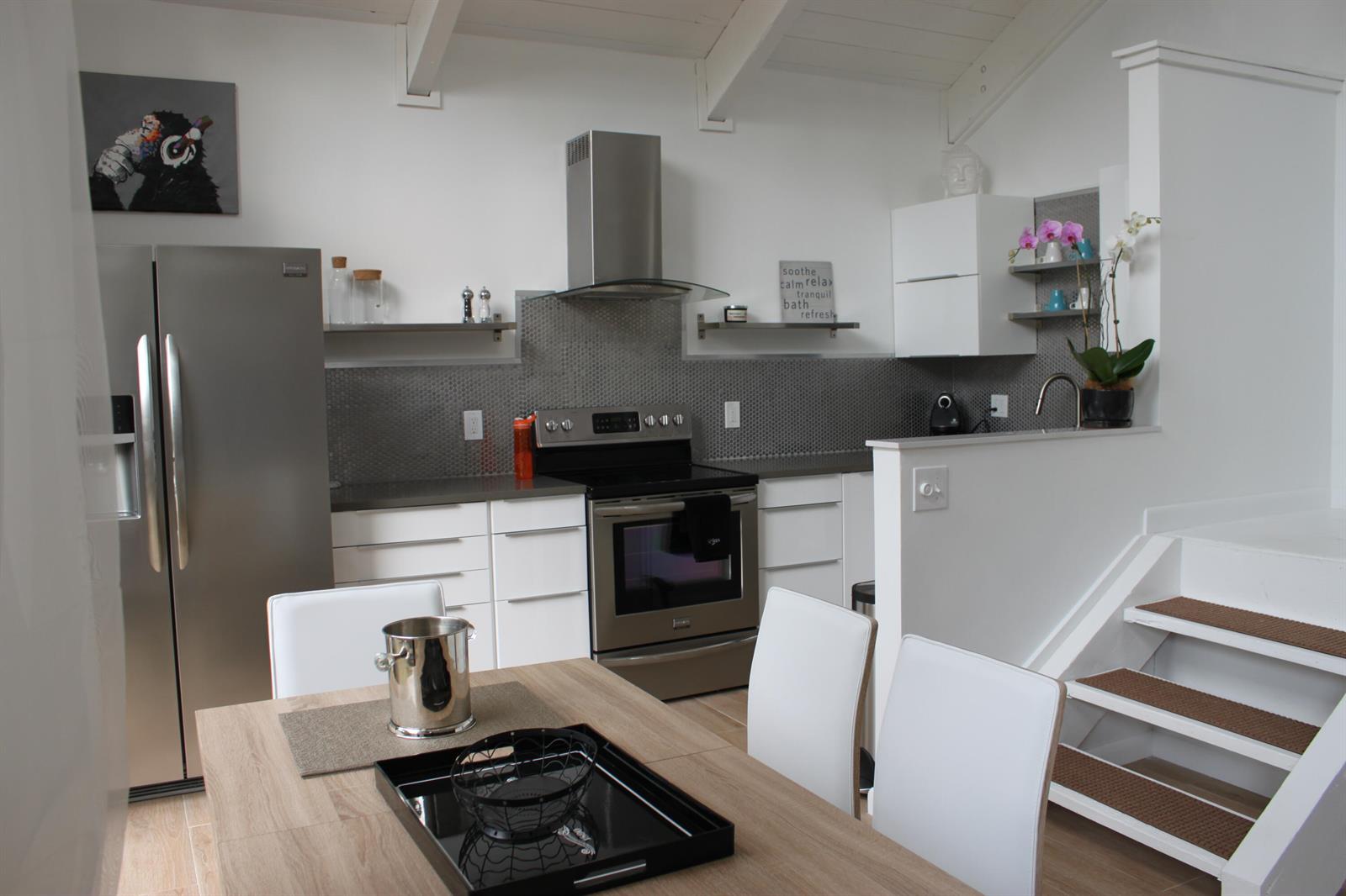 A modern kitchen features white cabinets, stainless steel appliances, a gray tiled backsplash, and stairs — 1605 S Us Hwy One, Jupiter FL 33477, JUPITER, FL