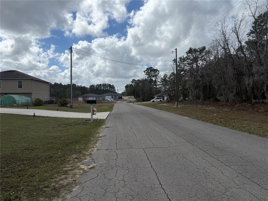 A paved road leads past a residential house and a wooded area under a cloudy sky — 0 SW 83RD CIRCLE UNIT 14, OCALA, FL