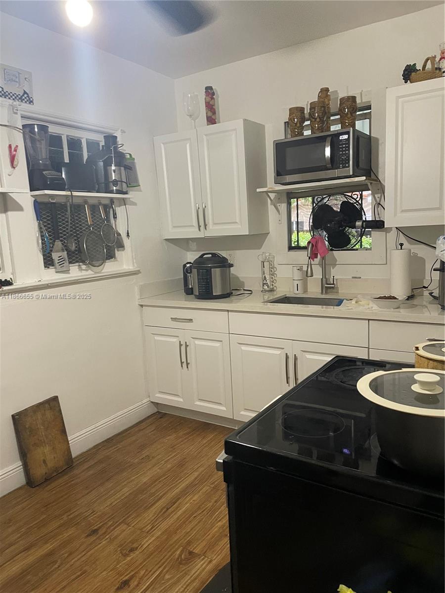A kitchen features white cabinets, a black stove, a microwave, and a window above the sink — 404 NW 23rd Ct, Miami FL 33125, MIAMI, FL