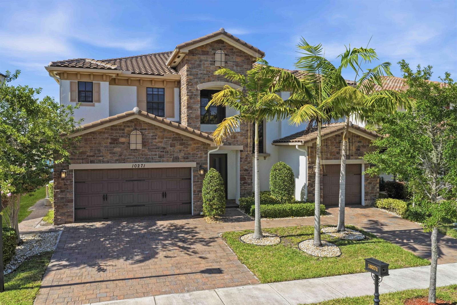 A two-story house with stone veneer, a tile roof, and a paved driveway with palm trees — 10271 Peninsula Place, Parkland FL 33076, PARKLAND, FL