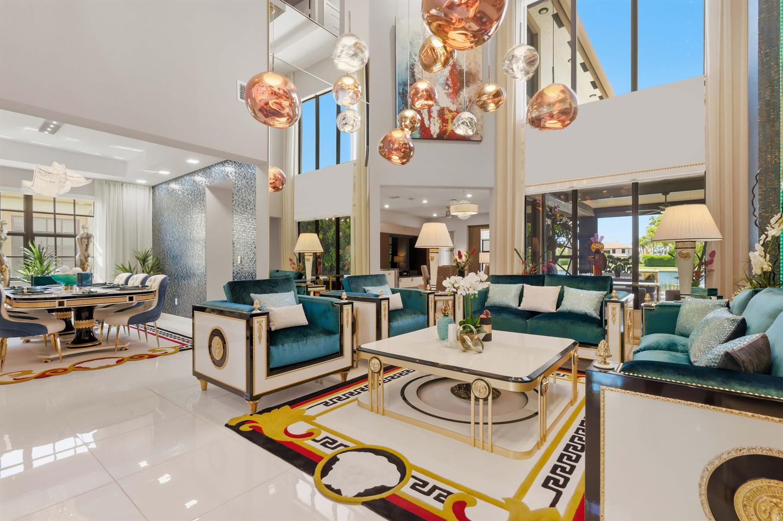 A luxurious living room features teal velvet furniture, a Greek key rug, and modern pendant lights — 10271 Peninsula Place, Parkland FL 33076, PARKLAND, FL