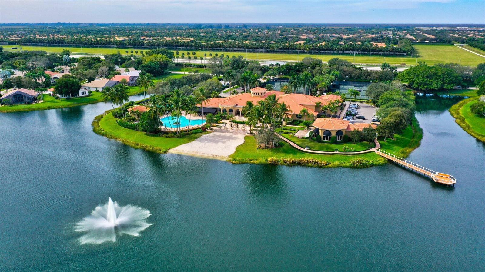 An aerial view of a clubhouse with a pool, sandy beach, and pier on a lake — 11564 Puerto Boulevard, Boynton Beach FL 33437, BOYNTON BEACH, FL