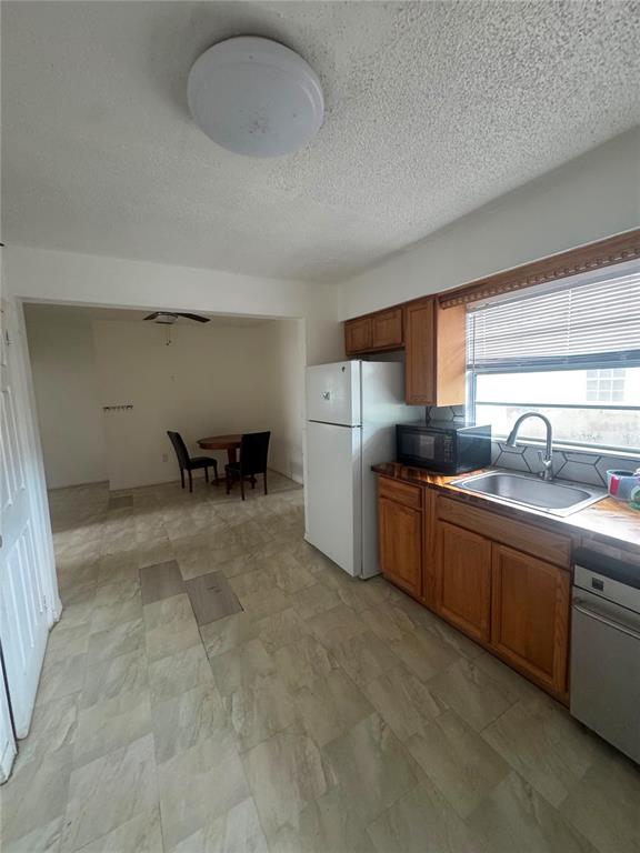 A kitchen with wood cabinets, a white refrigerator, and tile flooring leads to a dining area — 1808 17TH STREET E, PALMETTO, FL