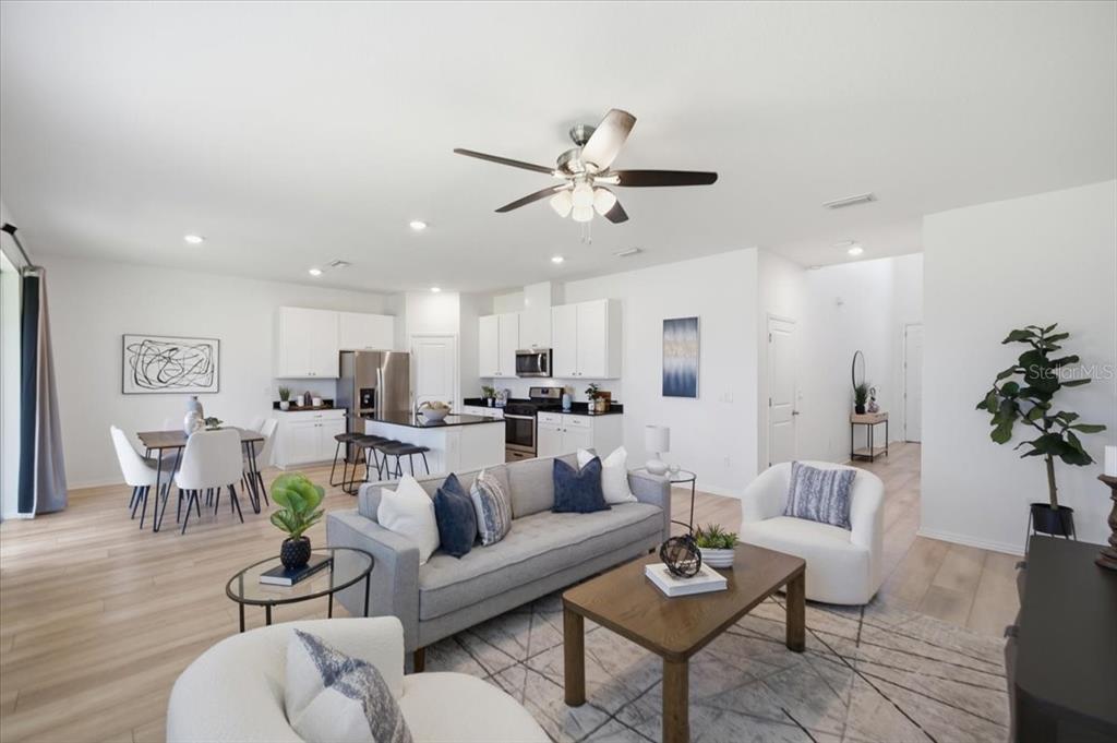An open-concept living room and kitchen featuring light wood floors, white cabinetry, and modern furniture — 5718 LOS ROBLES COURT, PALMETTO, FL