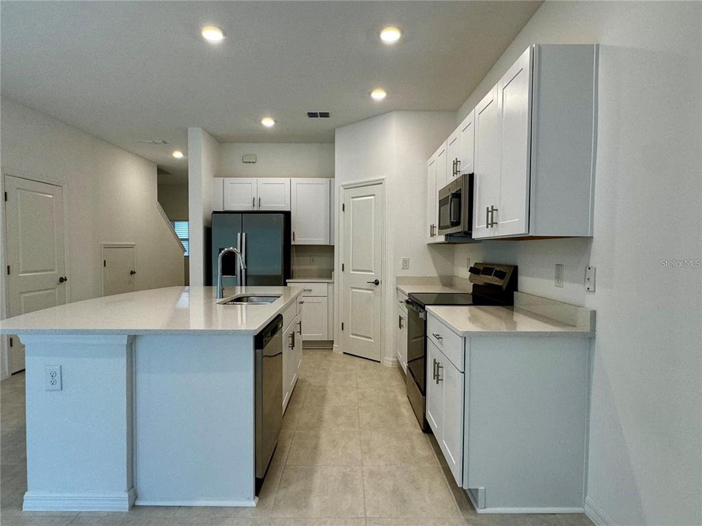A kitchen features white cabinets, stainless steel appliances, a center island, and light-colored countertops — 3037 CANARY AVENUE, DAVENPORT, FL