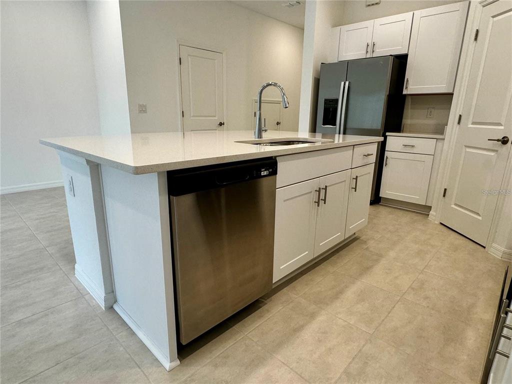 A kitchen island with a stainless steel dishwasher and sink sits before white cabinets — 3037 CANARY AVENUE, DAVENPORT, FL