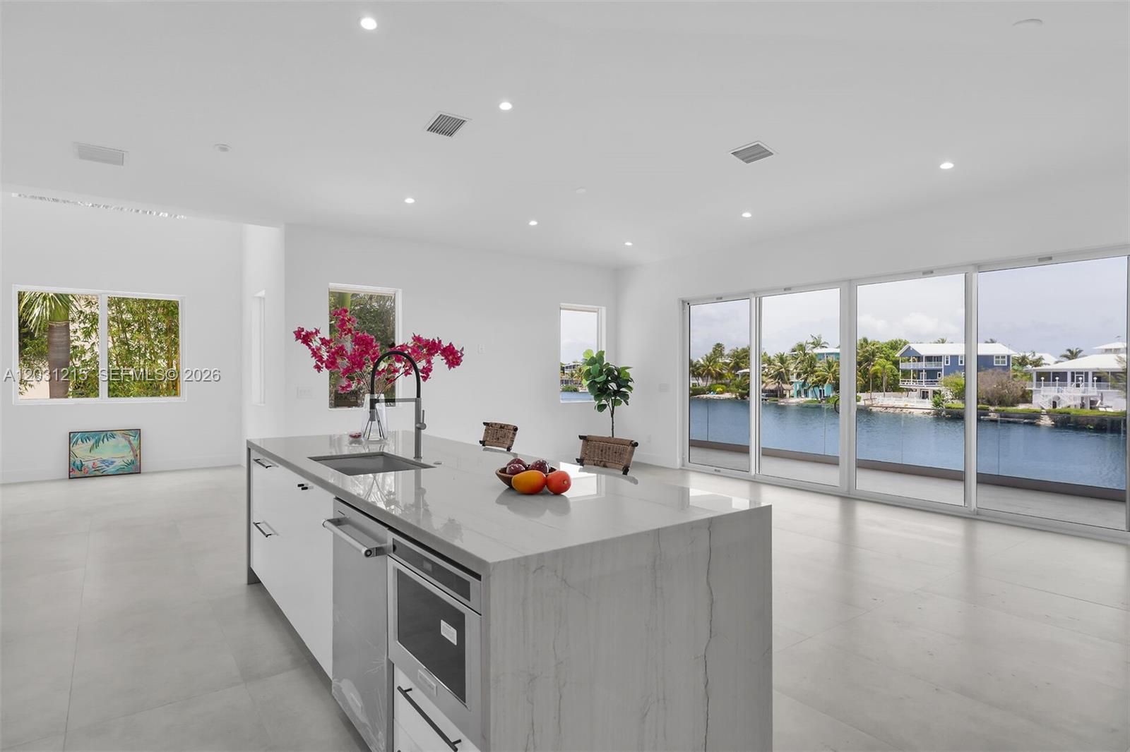 A modern kitchen island with a marble countertop overlooks a room with large glass doors — 38 N Bounty Ln, Key Largo FL 33037, KEY LARGO, FL