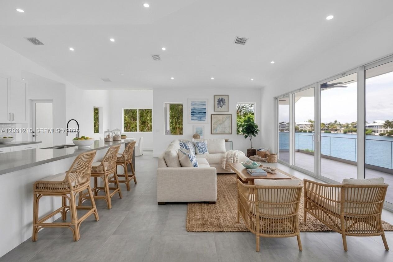 An open-concept living room and kitchen feature light-colored furniture, rattan chairs, and waterfront views — 38 N Bounty Ln, Key Largo FL 33037, KEY LARGO, FL