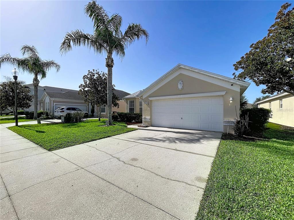 A beige single-story house features a two-car garage, a concrete driveway, and palm trees — 189 MINNIEHAHA CIRCLE, HAINES CITY, FL