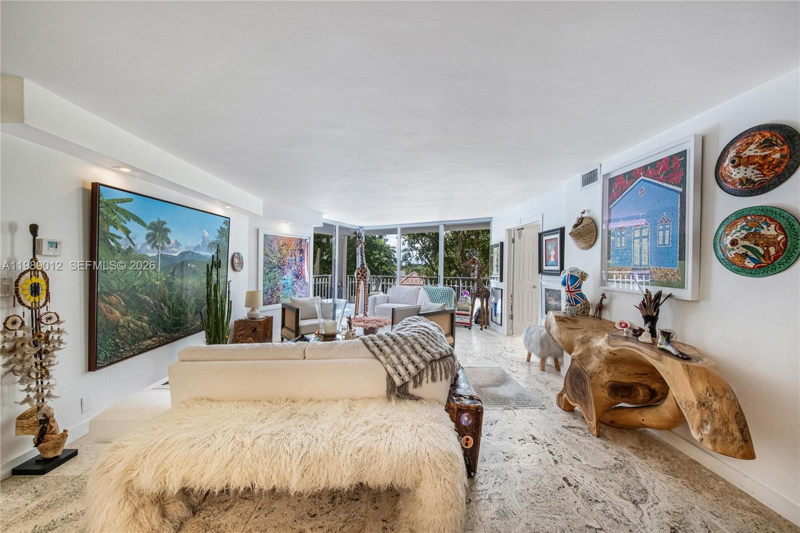 A bright living room features a white sofa, stone flooring, and eclectic wall art — 2000 Towerside Ter # 510, Miami FL 33138, MIAMI, FL