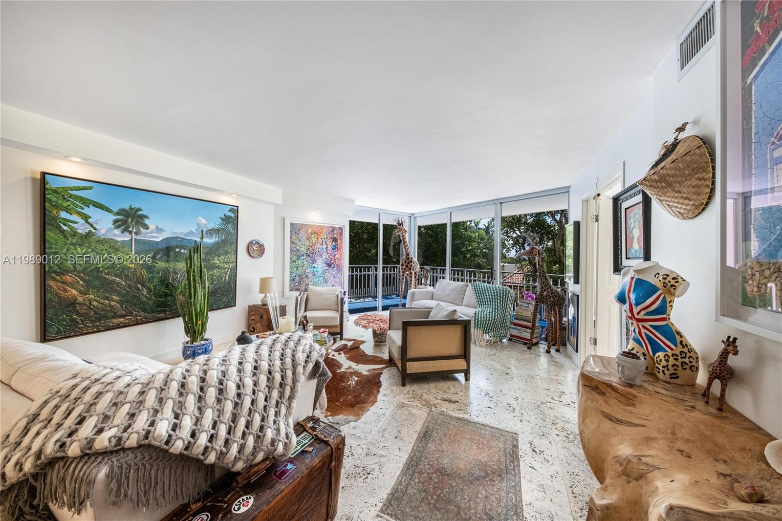 A living room features marble floors, large windows, eclectic decor, and a large landscape painting — 2000 Towerside Ter # 510, Miami FL 33138, MIAMI, FL
